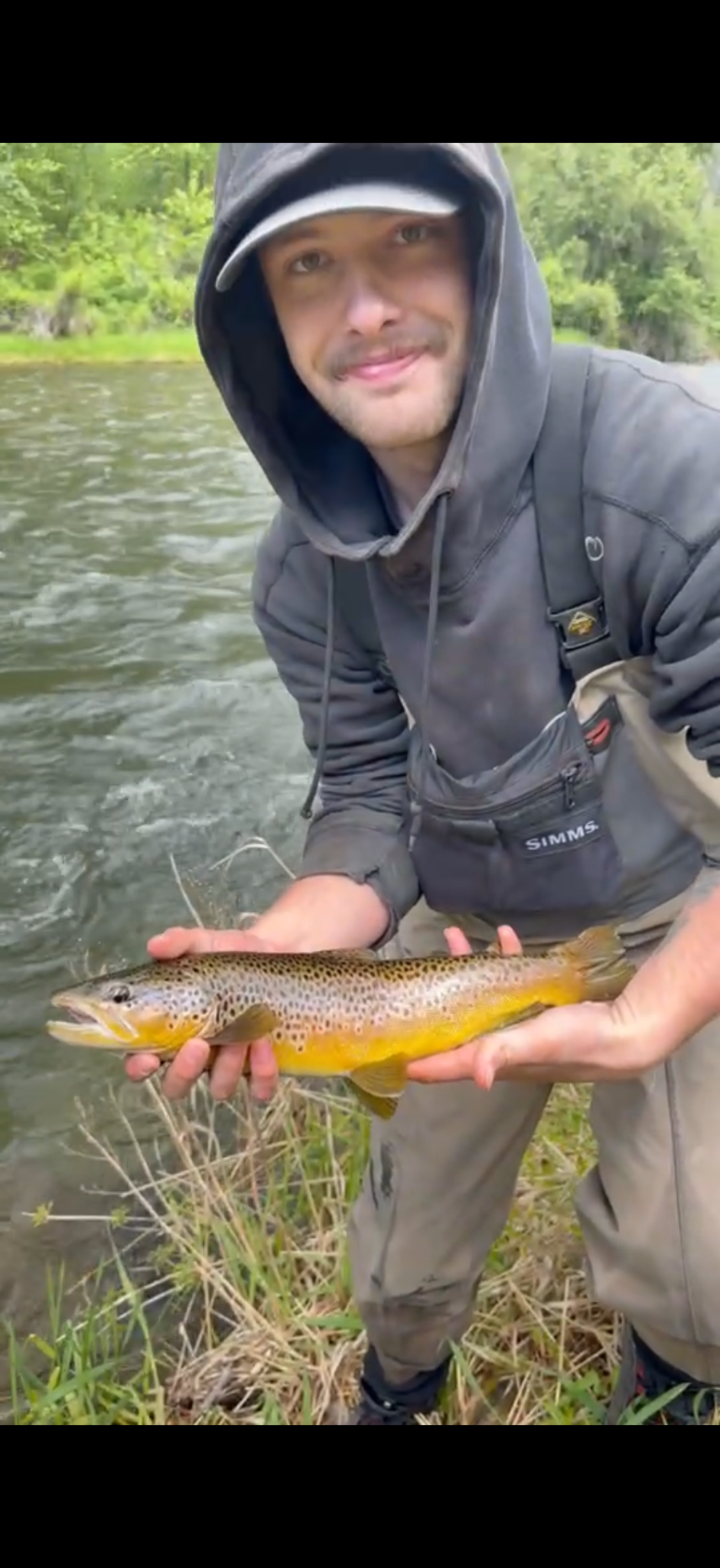 Joey outdoors by the river, holding a trout